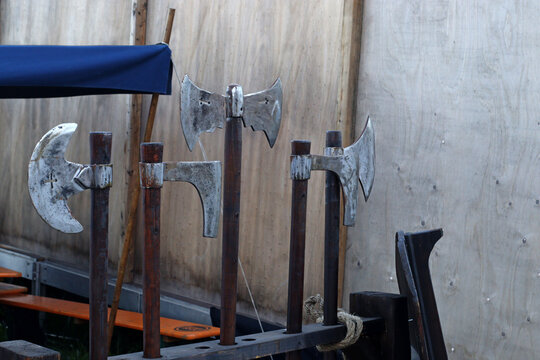 Medieval axes and polearms displayed on wooden stands at an outdoor fair, showing forged metal tools and weapons associated with traditional European warfare and craftsmanship.