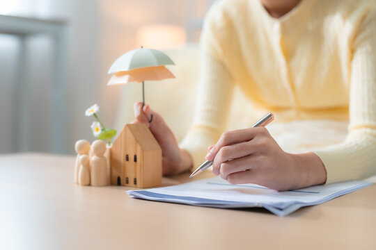 women reviewing home insurance documents beside wooden house, family figures, umbrella, representing property protection, coverage, financial security, risk management.
