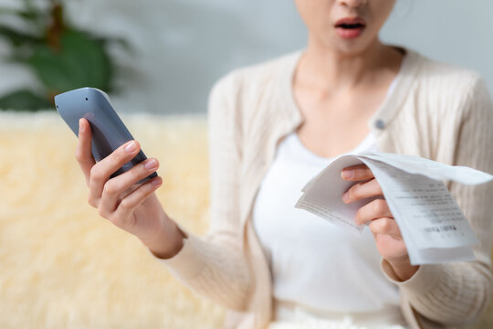 women looking shocked while checking bills, documents and calculator at home, representing financial stress, unexpected expenses, debt, budgeting problems, money management.