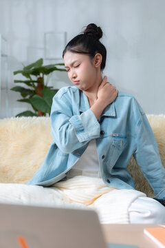 Woman sitting on sofa with laptop, touching sore neck from neck pain, shoulder tension, poor posture, office syndrome, remote work stress, ergonomic discomfort, health care at home.