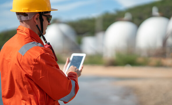 Industrial worker uses digital tablet to check operational information near storage tanks during outdoor facility inspection, maintenance, safety monitoring, energy operations.