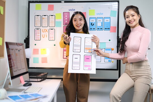 Young woman developer presenting UX/UI mobile app design wireframes to a colleague, discussing layout and prototyping ideas.