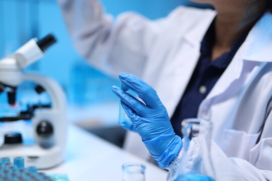 Scientist analyzing liquid sample in laboratory research. Scientist wearing protective gloves and glasses holding a test tube with blue liquid, conducting experiment in a research lab.