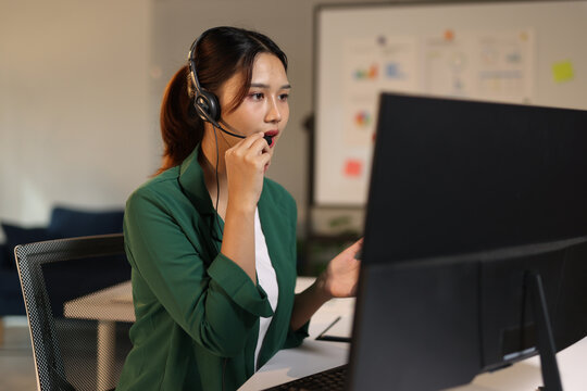 Asian woman call center agent or customer service representative working with a headset and computer in office.