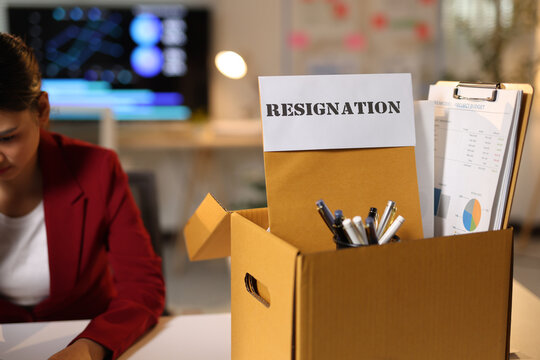 Employee resigning from job leaving office with box. Employee packing personal items into a cardboard box after resigning from an office job.