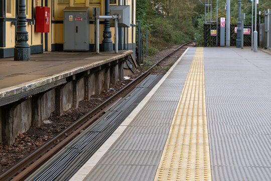 Far end of a railway station platform with tactile paving beside the track