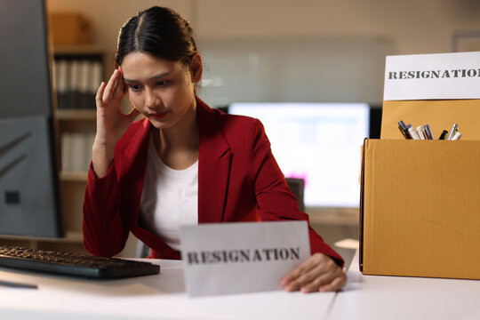 Young woman feeling stressed and burnt out at her office desk, preparing to resign while working late.