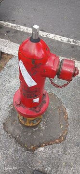 A bright red fire hydrant pillar with yellow accents at its base, installed at the edge of a paved road.
