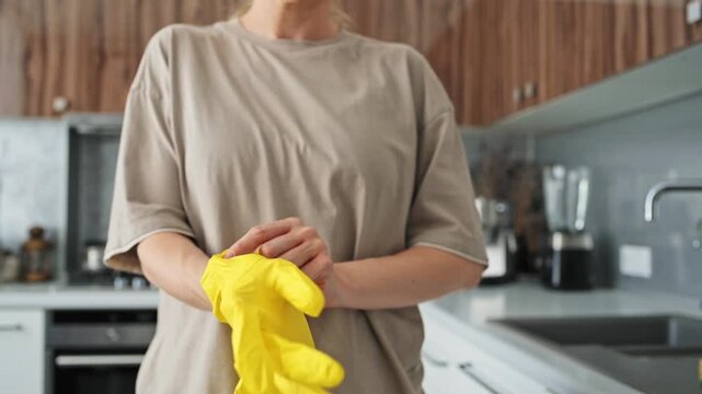 Yellow rubber gloves pulled on by hands in kitchen, preparing for household cleaning. Protective gloves support hygienic routines, surface care, dishwashing, and practical home maintenance tasks