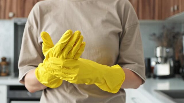 Woman checks fit of yellow rubber gloves inside kitchen before cleaning. Bright protective handwear highlights practical safety, hygiene and readiness for household maintenance activities