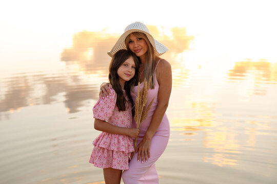 Mother And Daughter Sharing Embrace Beside Sunset Lake