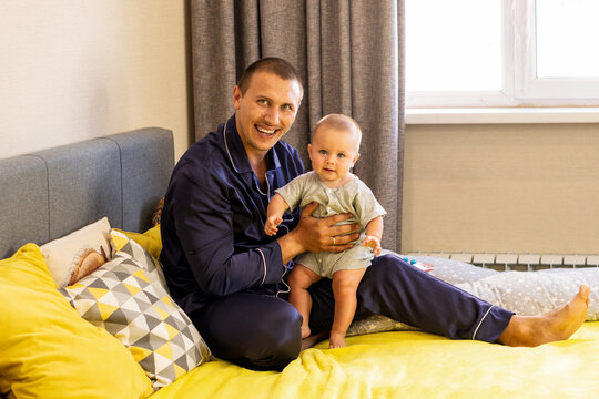 Smiling Father Holding Baby Son On Bed At Home