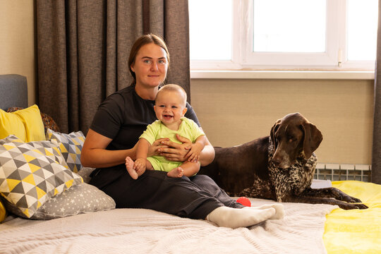 Mother Holds Laughing Baby Beside German Shorthaired Pointer
