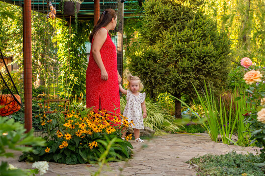 Mother Walking With Young Daughter Through Summer Flower Garden