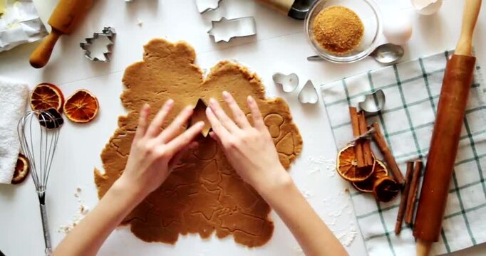 Woman hands cutting out christmas gingerbread cookies from rolled dough on white surface.