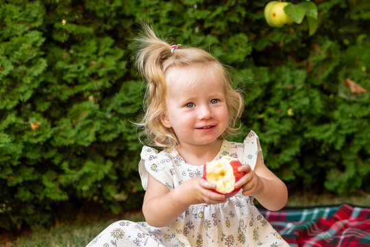 Smiling Young Girl Holding Bitten Red Apple Outdoors