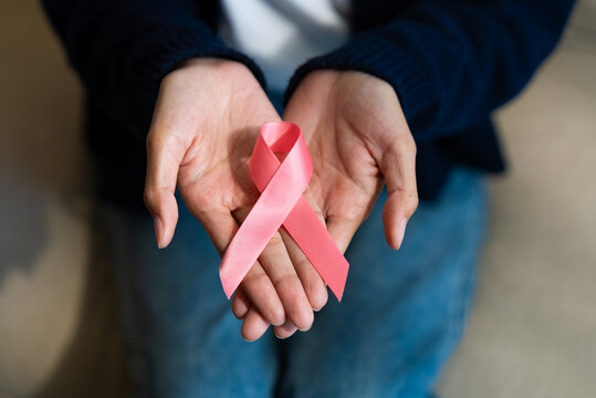 Close-up of a woman's hands gently holding a pink ribbon for breast cancer awareness campaign. Asian female patient support, healthcare, and hope concept.