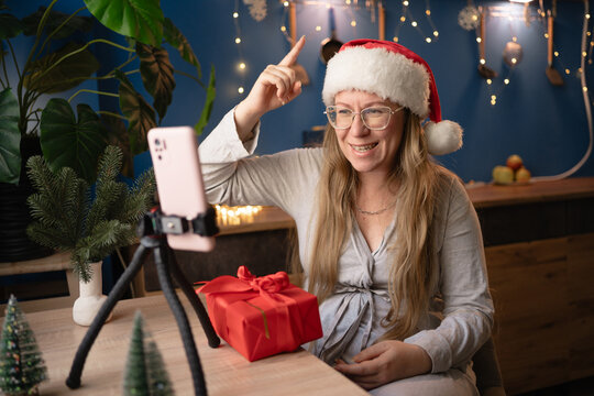 New Year, livestreaming, blogging and Merry Christmas. woman blogger influencer in Santa hat raising finger in eureka sign recording video blog using smartphone on tripod at home.
