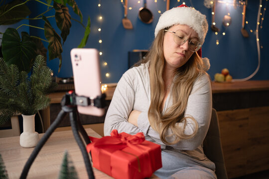 New Year, livestreaming, blogging and Merry Christmas. Resentful woman blogger influencer in Santa hat crossed arms on chest recording video blog using smartphone on tripod at home.