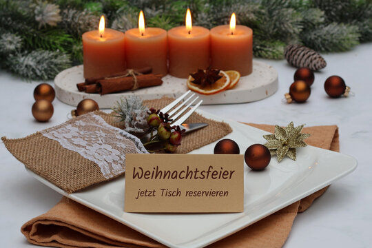 Festliche Tischdekoration zu Weihnachten mit vier brennenden Adventskerzen, Teller, Besteck und einer Karte mit der Aufschrift Weihnachtsfeier jetzt Tisch reservieren.