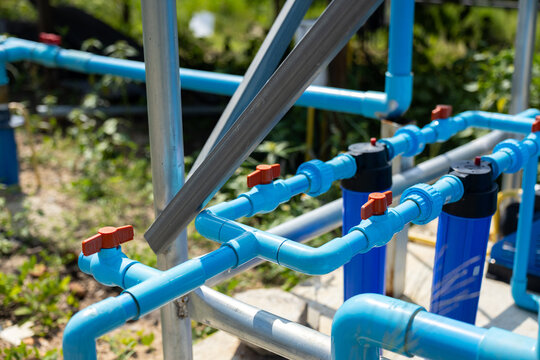 Blue water filtration pipe network outdoors with valves, filter housing, and metal support frame