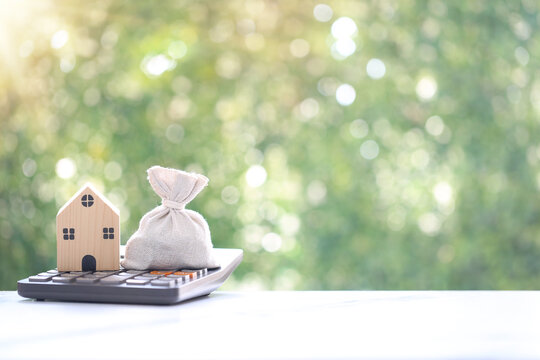 Calculating interest payments, Wooden house model and money bag on calculator for home finance and investment planning