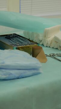Surgical team arranging sterile gauze, folded towels, metal instruments, and basins on teal drape during careful preoperative setup with gloved hands in clinical operating room lighting