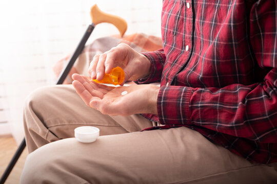 Older Person Holding Medication Bottle and Pill at Home