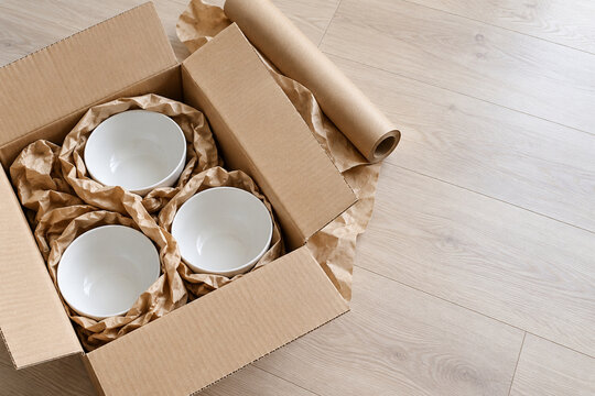 Weisse Keramikschalen mit Packpapier im Umzugskarton