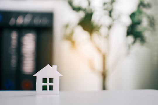 Small house model representing real estate investment on wooden desk with blurry office background for property development and home mortgage concept