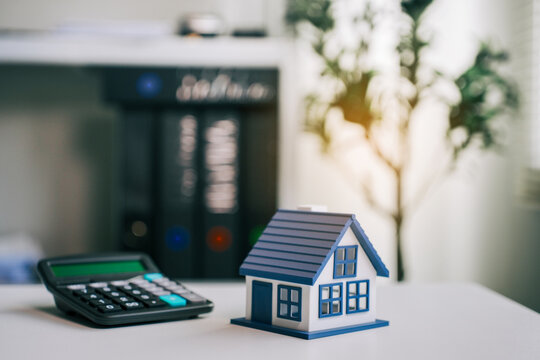 Model house and black calculator on desk representing real estate investment, home loan planning, mortgage financial analysis and property insurance concepts