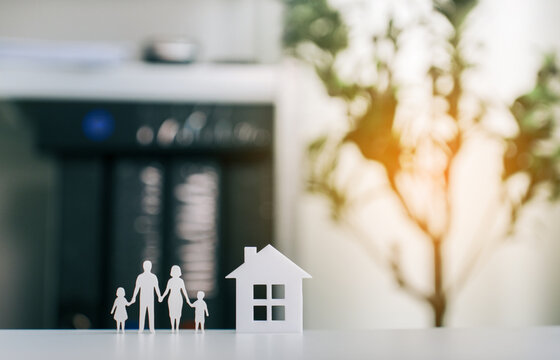 Family paper cutout standing next to model house representing property ownership investment financial stability and home mortgage insurance plan in cozy home office setting