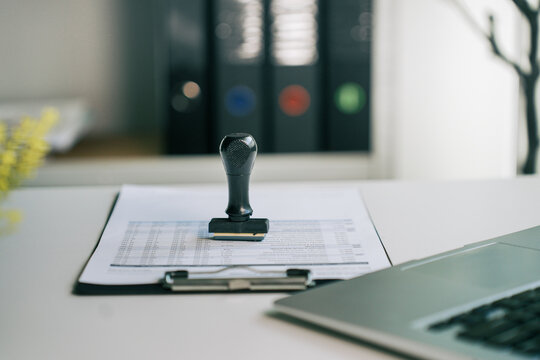 Rubber stamp on financial document report on office desk with laptop computer, business contract approval and administrative compliance concept for corporate accounting