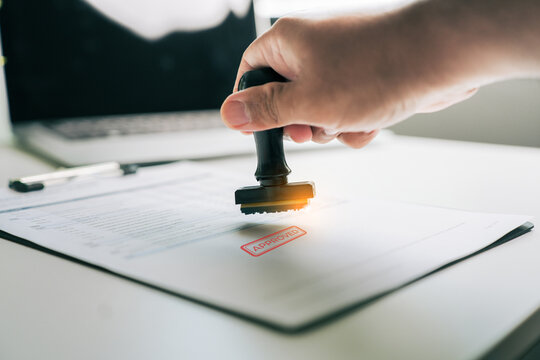 Approved stamp on legal contract document held by businessman in office, official business agreement verification concept
