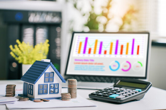 Real estate investment planning with miniature house model, coins, calculator, and financial growth charts on laptop for property market analysis and mortgage savings concept