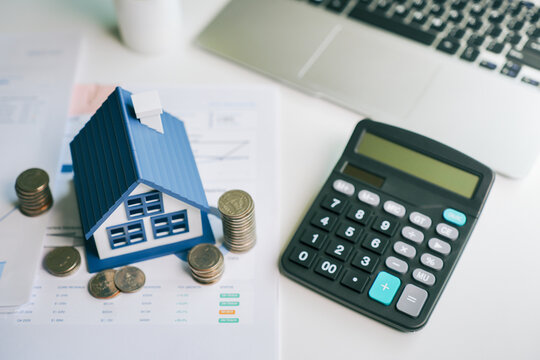 Real estate investment model house with stack of coins and calculator for property tax planning and financial loan calculation on office desk report