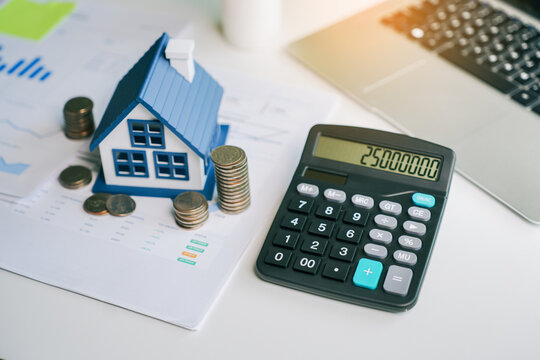 Real estate investment calculator with model house and stack of coins for mortgage interest rate planning and property financial analysis on office desk