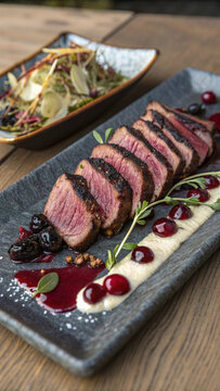 Photorealistic vertical venison heart slices with juniper crust cherry glaze celeriac puree charred salsify and crispy buckwheat