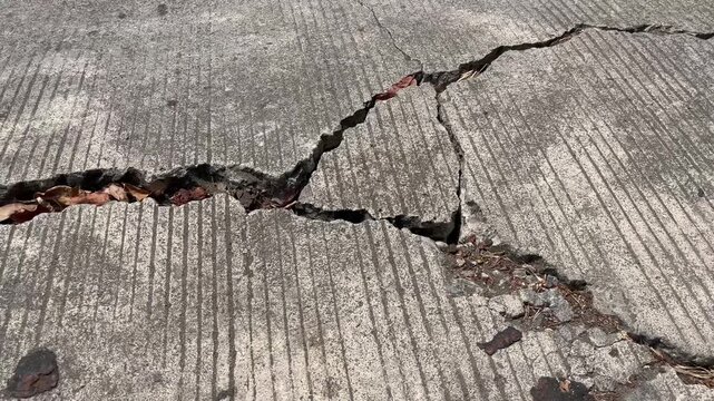 Close up of broken concrete road surface with deep cracks