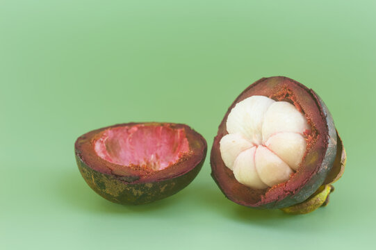 Cut mangosteen halves with white flesh and empty peel on green background