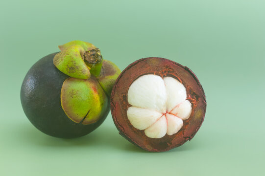 Whole mangosteen and half with white flesh on mint green background