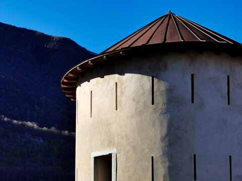 Historic stone defense tower with arrow slits and conical roof against mountains in Bellinzona