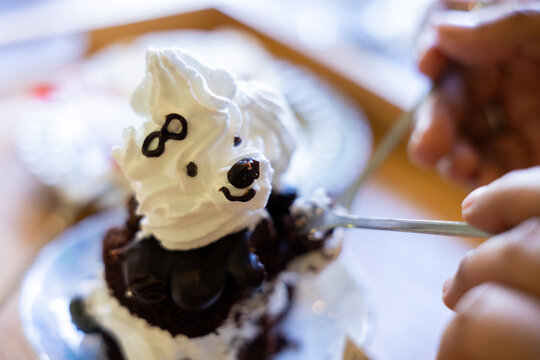 White whipped cream dessert with playful face decoration, served on plate while person adds chocolate detail