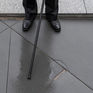 Cane tip and polished black boots on rain-wet slate paving, a somber and dignified scene for remembrance day and commemorative layouts