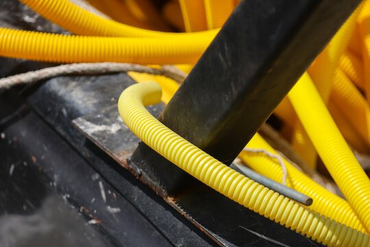 Yellow corrugated conduit surrounds black pipe and metal cable in industrial construction closeup with rugged texture and vivid color contrast