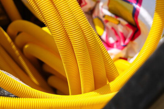 Yellow corrugated hose coils create textured abstract pattern around colorful fabric, with curved plastic tubing filling frame and bright industrial detail