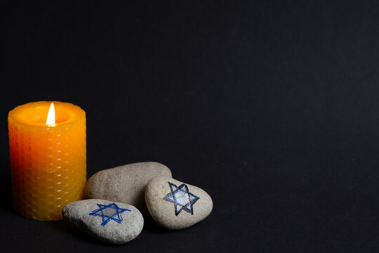 Holocaust remembrance symbol with Star of David stones and candle on dark background