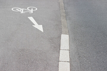 Fototapeta premium Bicycle lane marking on asphalt road with directional arrow indicating bike path, concrete curb visible along the edge of the lane
