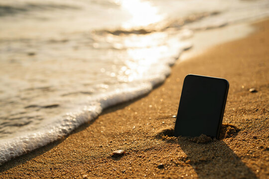 Smartphone stuck in sand on a beach shore near ocean waves photo illustration