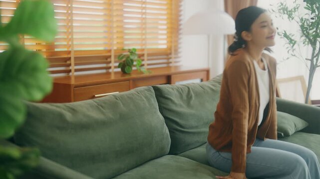 Relaxed young Asian woman enjoying rest on comfortable sofa, calm attractive girl relaxing on couch, breathing fresh air with eyes closed, meditating at home